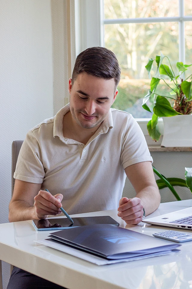 Pit Meissner sitzt lächelnd am Schreibtisch. Sein Blick ist auf einen Notizblock gerichtet. In der Hand hält er einen Stift.